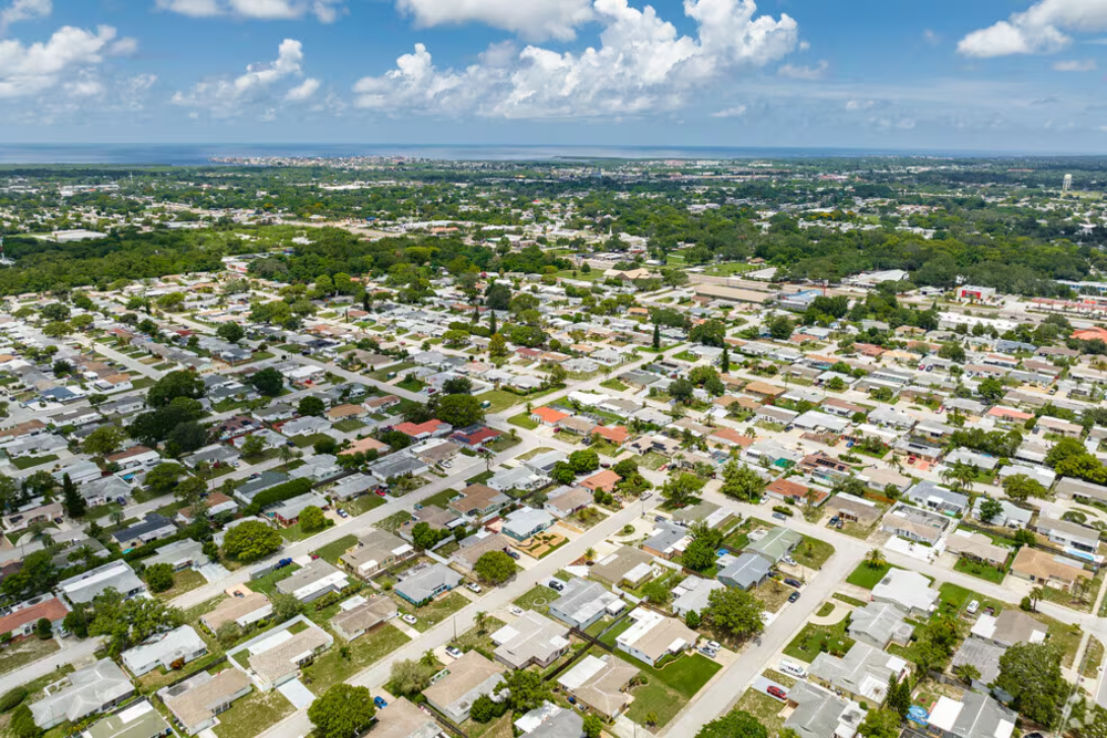 Elfers Florida Aerial view of a suburban neighborhood with grid streets, single-family homes, and many trees under a blue sky with clouds.