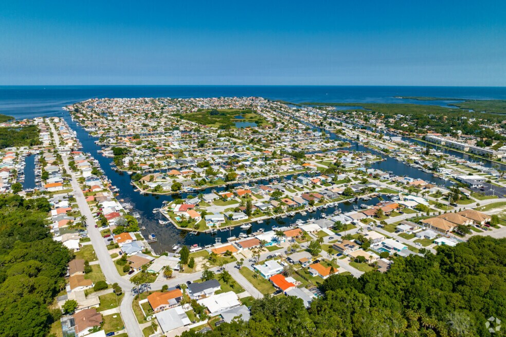 New Port Richey Aerial view of a coastal canal-front neighborhood with numerous houses, water channels, and a distant ocean horizon.