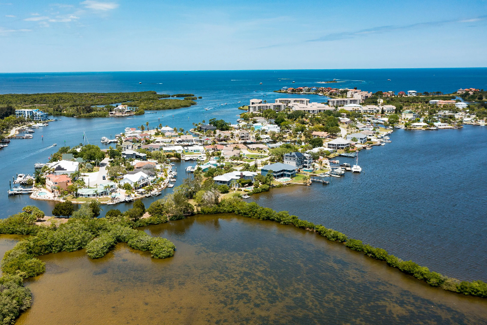 Port Richey Aerial view of a coastal residential neighborhood with houses along canals, boats docked at piers, and the blue sea in the background.