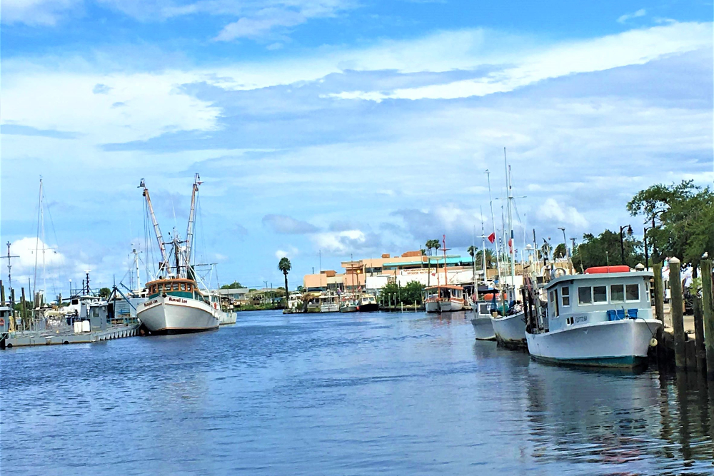 Tarpon Springs fl Boats docked along a calm blue canal in a coastal marina with a clear sky and distant buildings ahead.