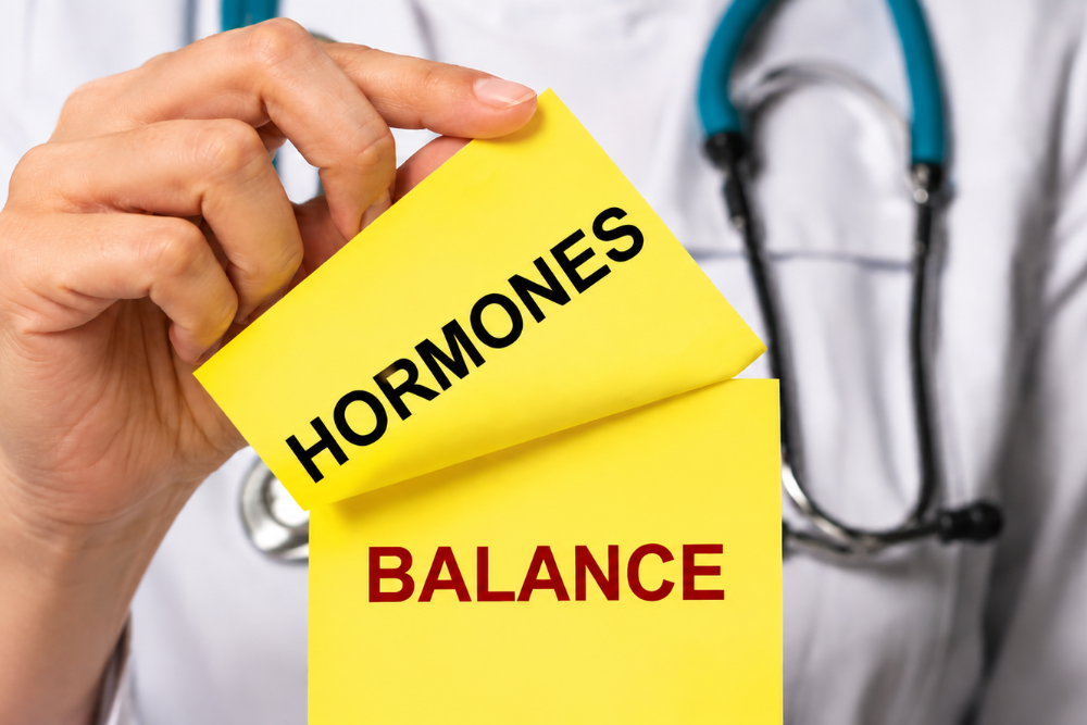 Doctor holds yellow notes reading 'HORMONES' and 'BALANCE'—symbolizing hormonal balance.